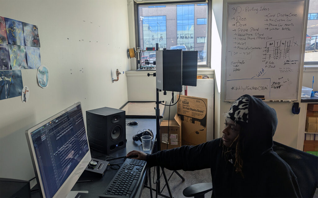 A Drexel University student sits at a computer desk playing a song off of a desktop computer