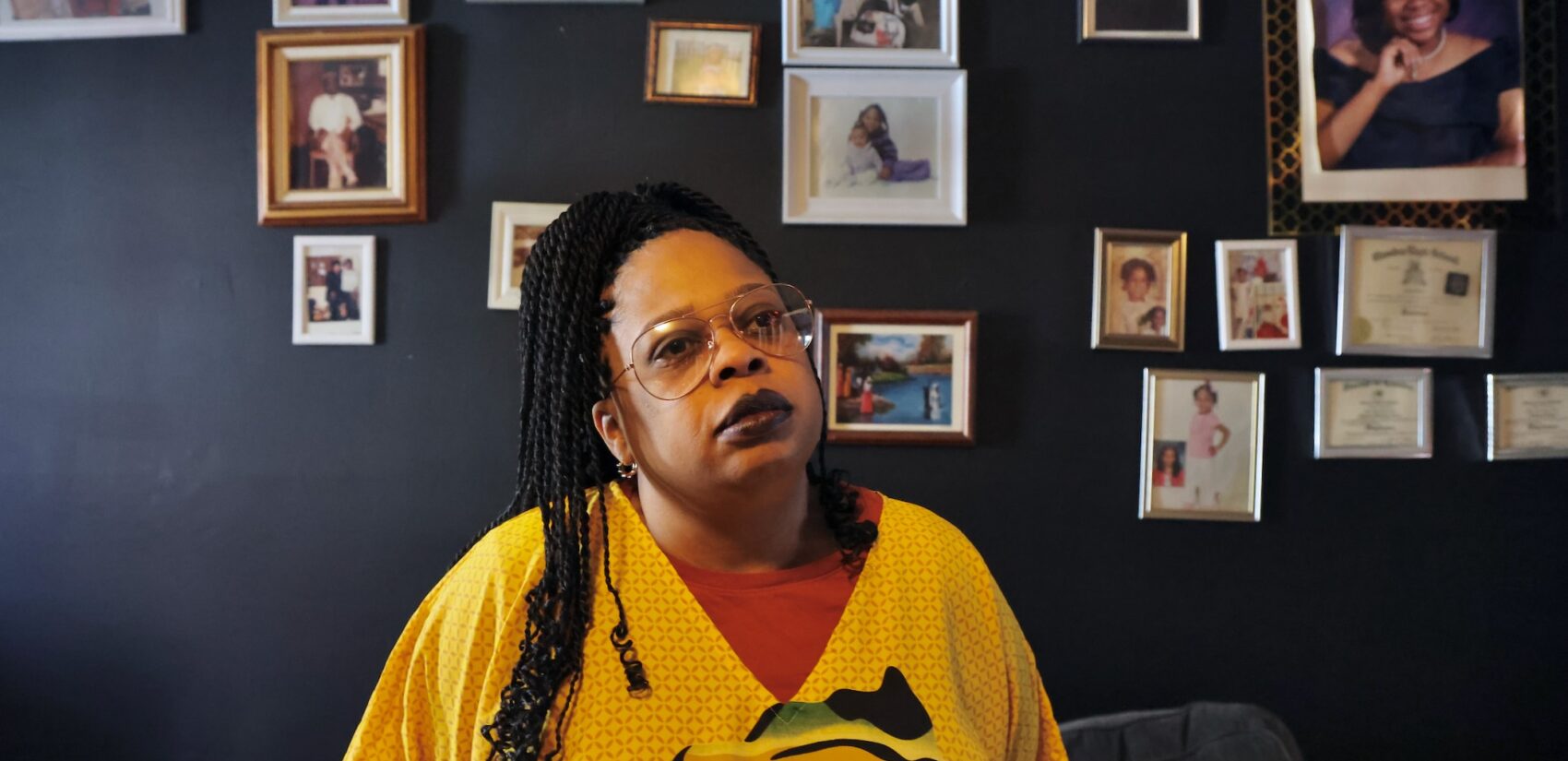 Aliyia Jones stands in front of a wall of family photographs