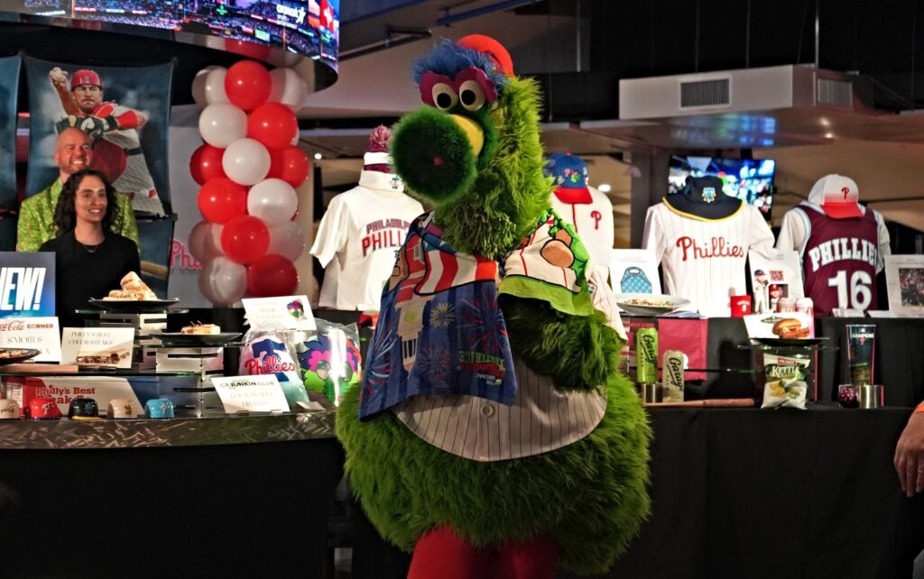 phanatic-stadium-n-kariuki-2025-03-31 The Phillie Phanatic showing off all of the merchandise set up on a table behind them