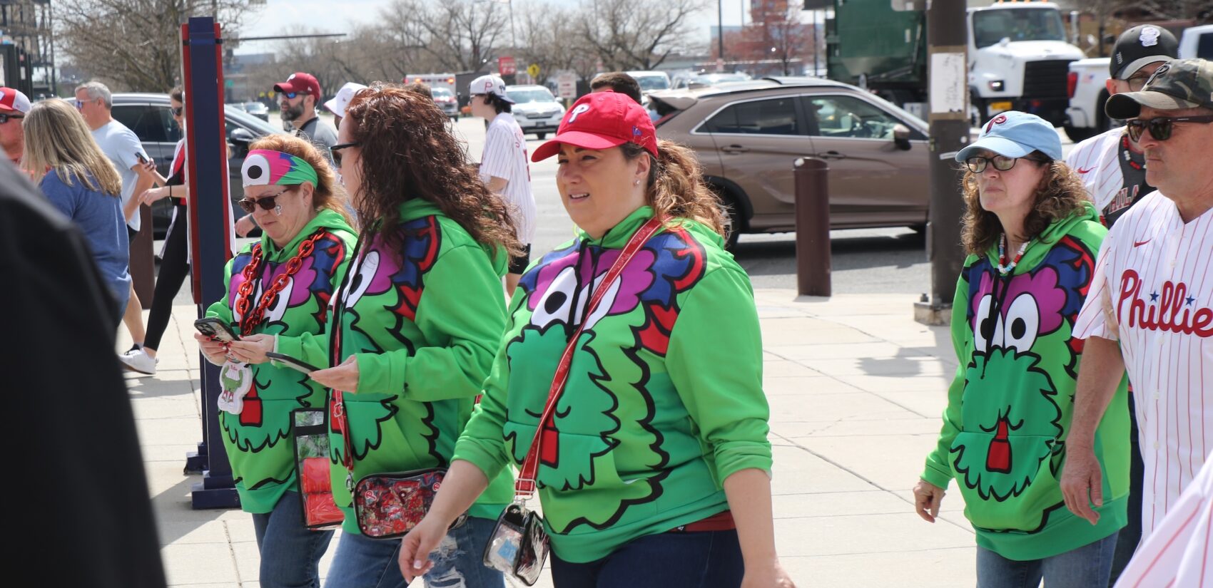 A group of women walking into the stadium wearing matching green Phillie Phanatic sweatshirts