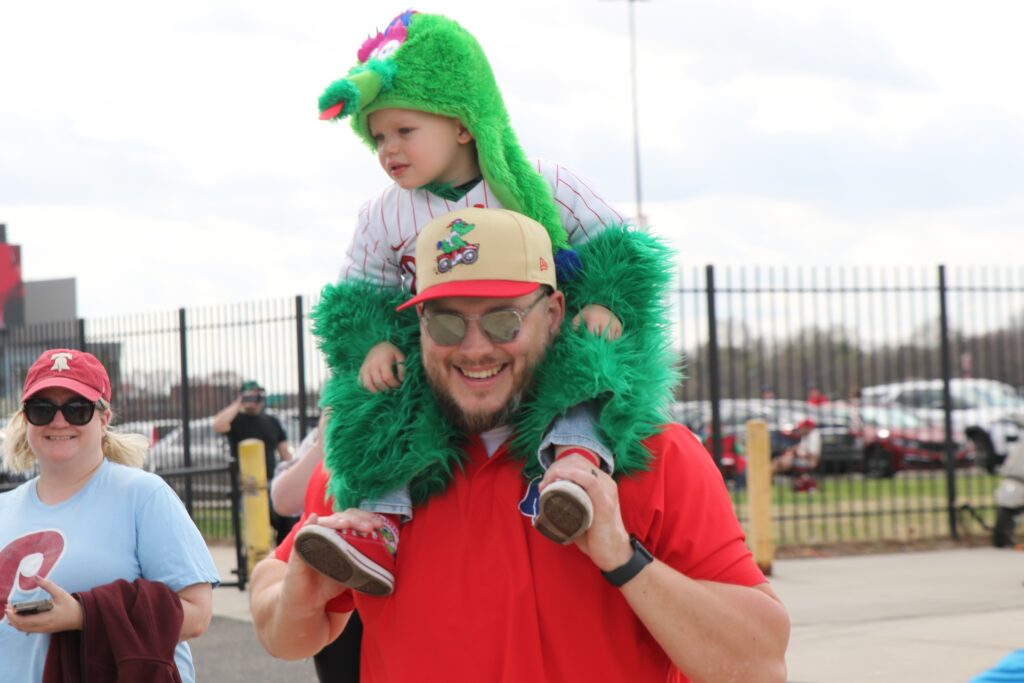 phillies-home-opener-c-sharber-2025-03-31-7 A man holding a small child on his shoulders who is wearing a Phanatic costume