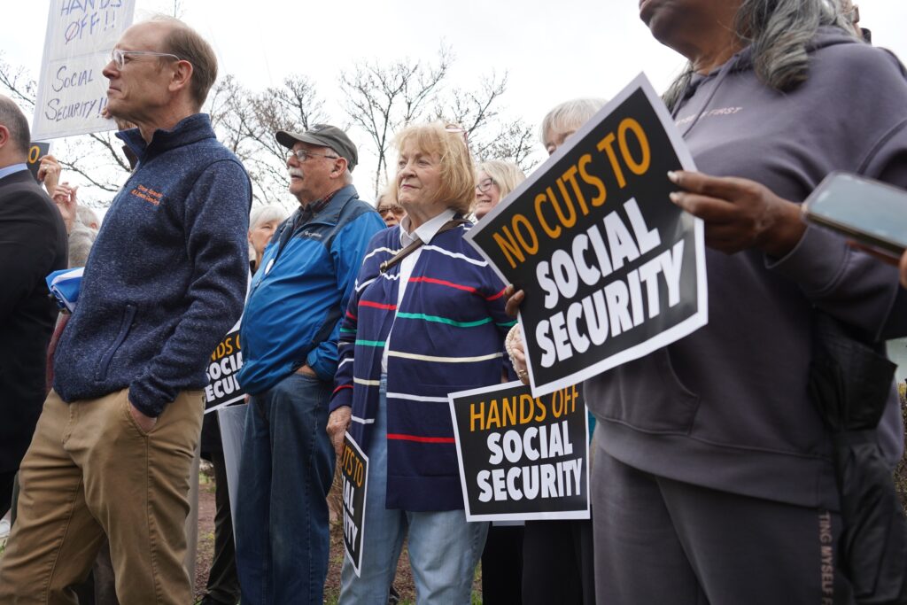 Seniors rallying, with signs reading NO CUTS TO SOCIAL SECURITY and HANDS OFF SOCIAL SECURITY