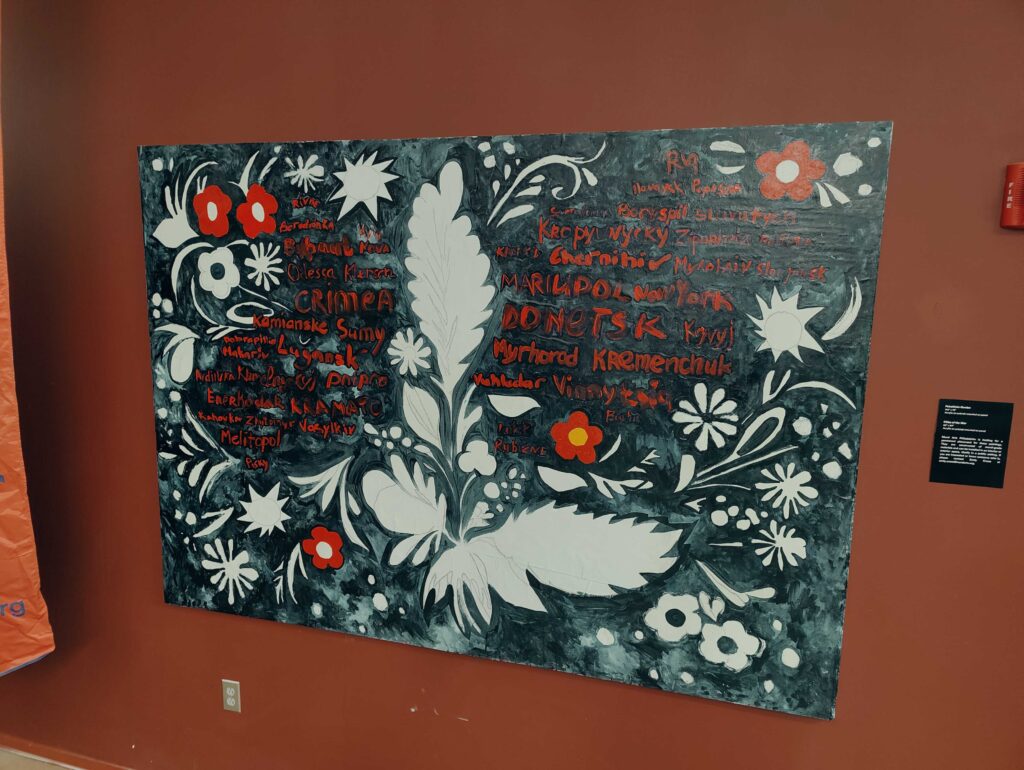 A black, white and red painting of flowers and plants hangs on a red wall.