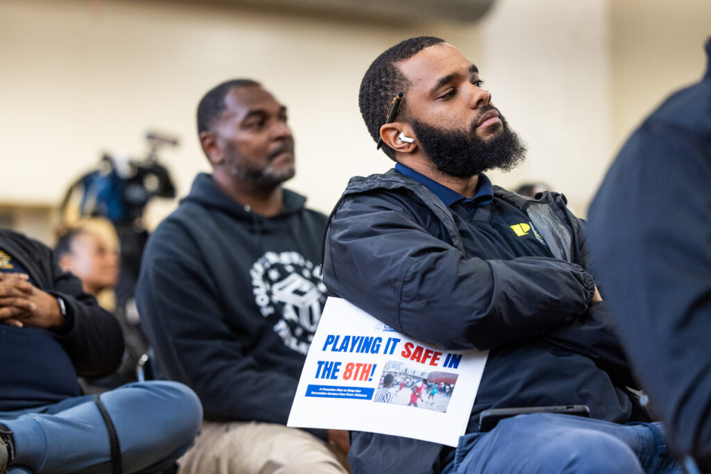 04-15-2025-k-paynte-lonnie-young-rec-center-town-hall-9 residents sitting, one holding a paper docket reading PLAYING IT SAFE IN THE 8TH!
