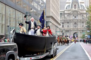 Actors portraying George Washington and his crew on the boat crossing the river, being driven down Broad Street during a parade