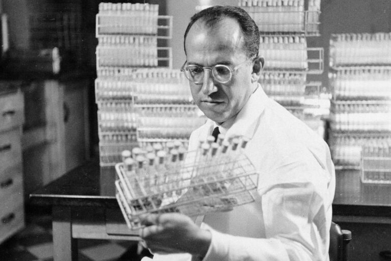 Jonas Salk holds a rack of test tubes