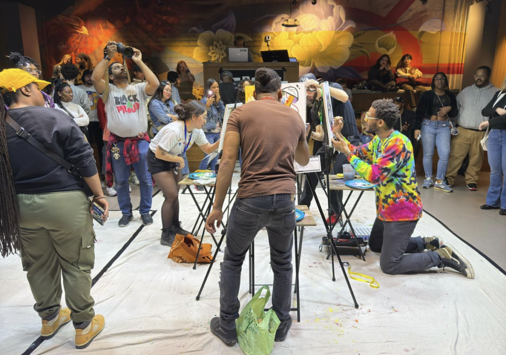 arts-battle-bp-2025-04-08 2 artists painting facing each other , with a crowd circled around them