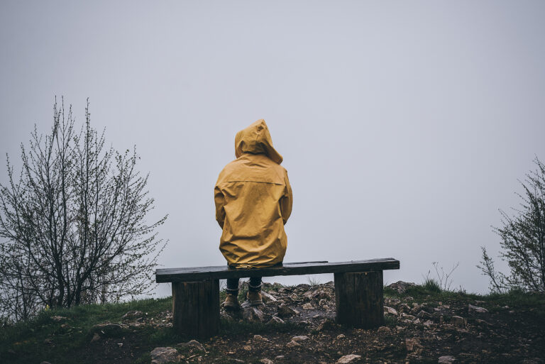 Sad depressed woman sitting on bench in raincoat