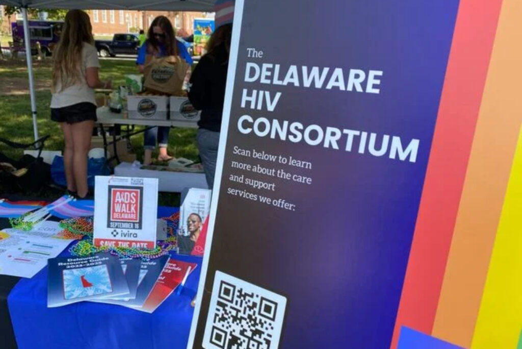 a poster reads DELAWARE HIV CONSORTIUM under a tent at an event