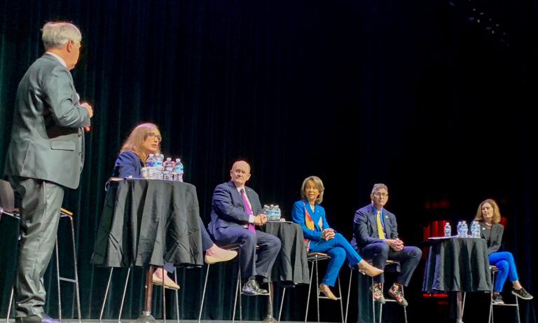 A moderator on stage with 5 panelists for the town hall