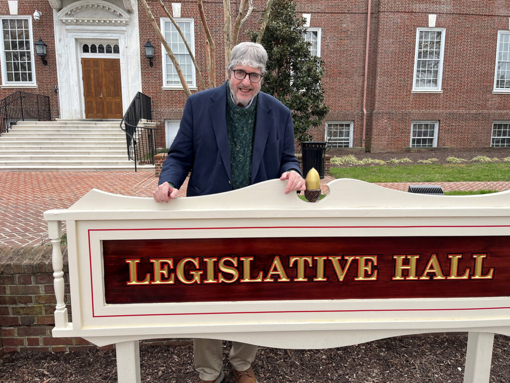 John Flaherty posing for a photo at the sign for Legislative Hall