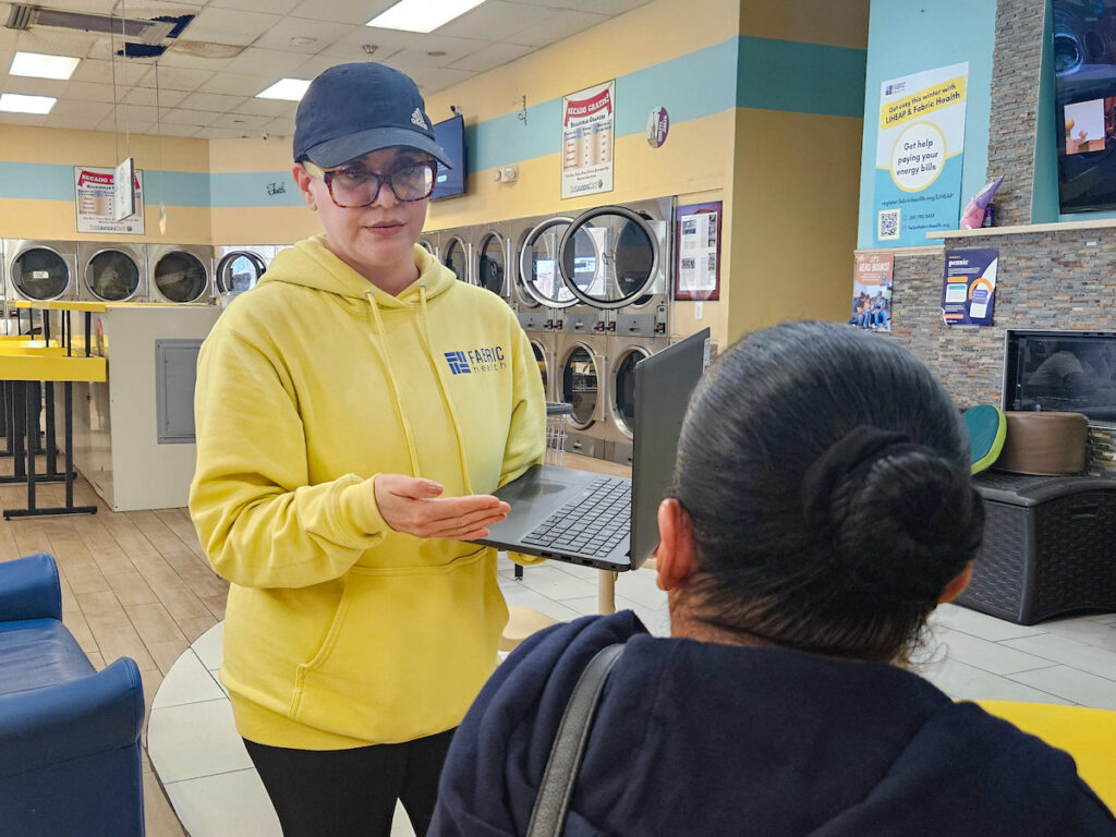 laundromat-health-outreach-NL042125-01 Outreach worker Mariela Tentsoglides speaking to woman at laundromat about healthcare