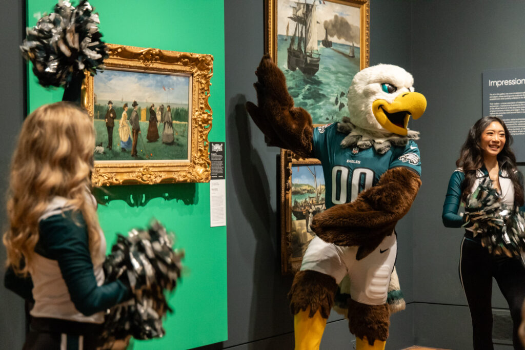 Swoop posing for a photo with a painting on the wall