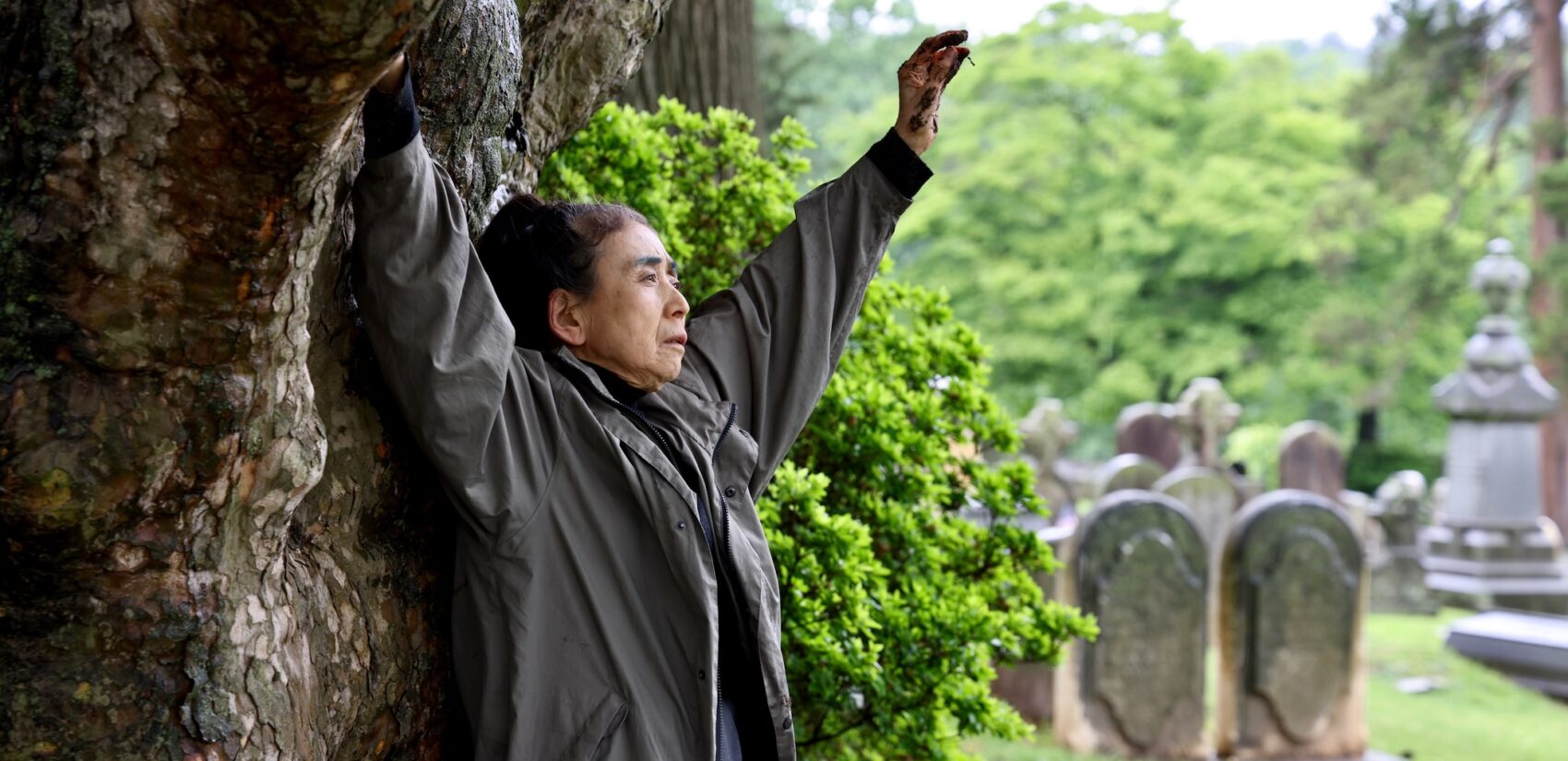 Eiko Otake raises her arms beneath a tree at Laurel Hill Cemetery for the Death and Arts Festival