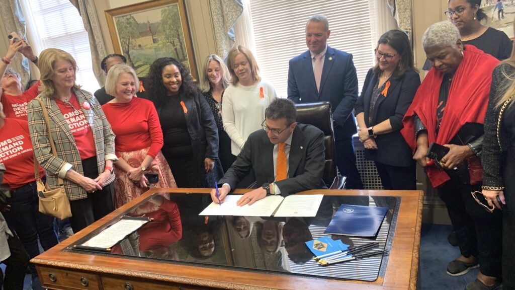 Meyer-Gun-violence-sign-s-mueller-2025-05-01 Matt Meyer signing a paper on his desk, surrounded by people