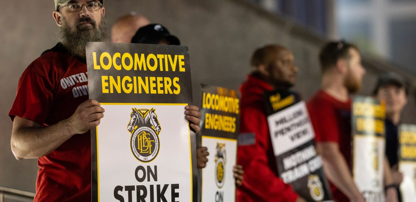 Union members from the Brotherhood of Locomotive Engineers and Trainmen form a picket line, with signs reading LOCOMOTIVE ENGINEERS ON STRIKE