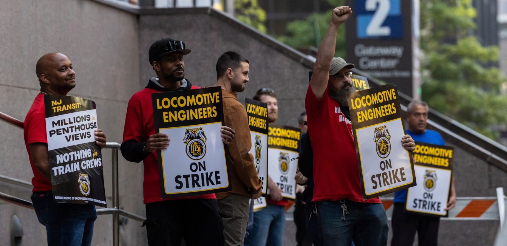 around 7 union members from the Brotherhood of Locomotive Engineers and Trainmen form a picket line, with signs reading LOCOMOTIVE ENGINEERS ON STRIKE