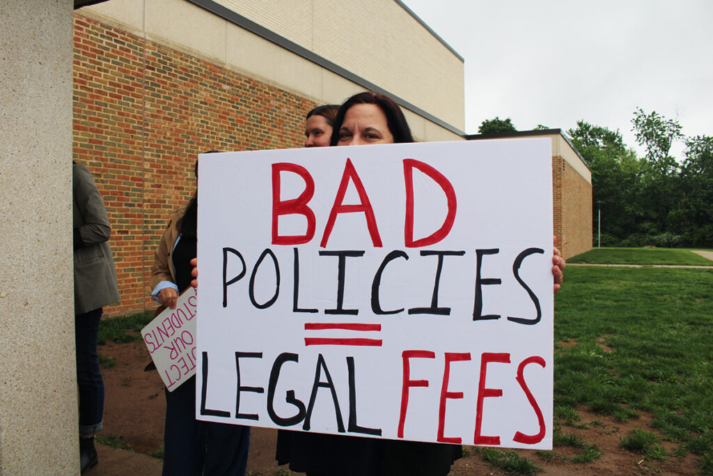 a parent protesting he possible appointment of Abram Lucabaugh as Centennial School District's new superintendent holds a sign reading BAD POLICIES = LEGAL FEES
