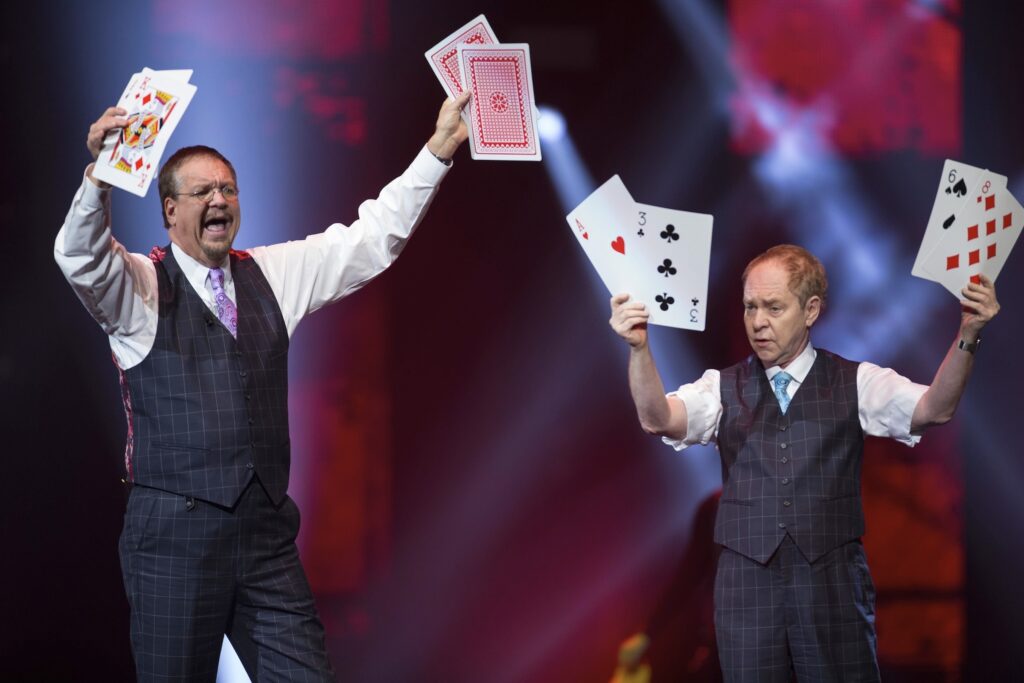 Penn and Teller on stage holding up oversized playing cards