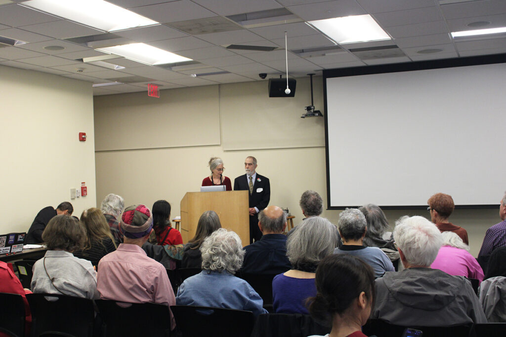 A man and a woman stand behind a podium in front of an audience