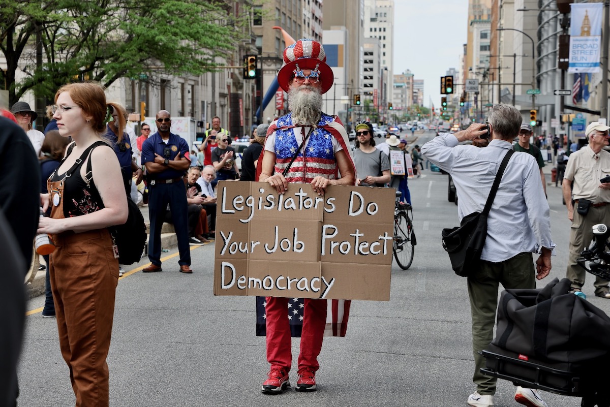 A man wearing an American flag carrying a sign during a May Day rally at Philadelphia City Hall
