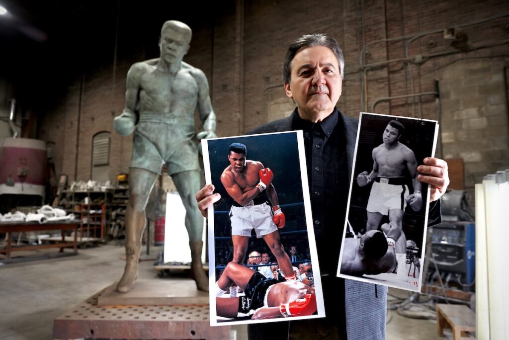 Zenos Frudakis posing with photos that inspire his Muhammad Ali statue