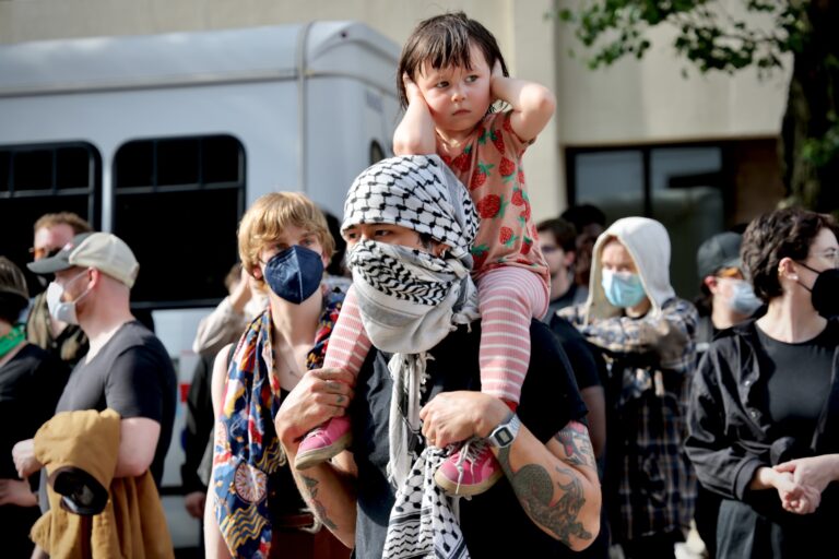 A 3-year-old girl perched on her father's shoulders covers her ears during a noisy protest outside the Federal Detention Center at 7th and Arch streets. About 200 people gathered to protest the activities of United States Immigration and Customs Enforcement arrests.