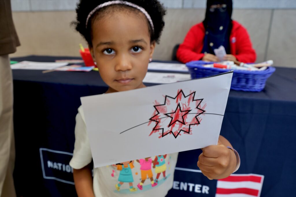 A young girl holds up a flag she made