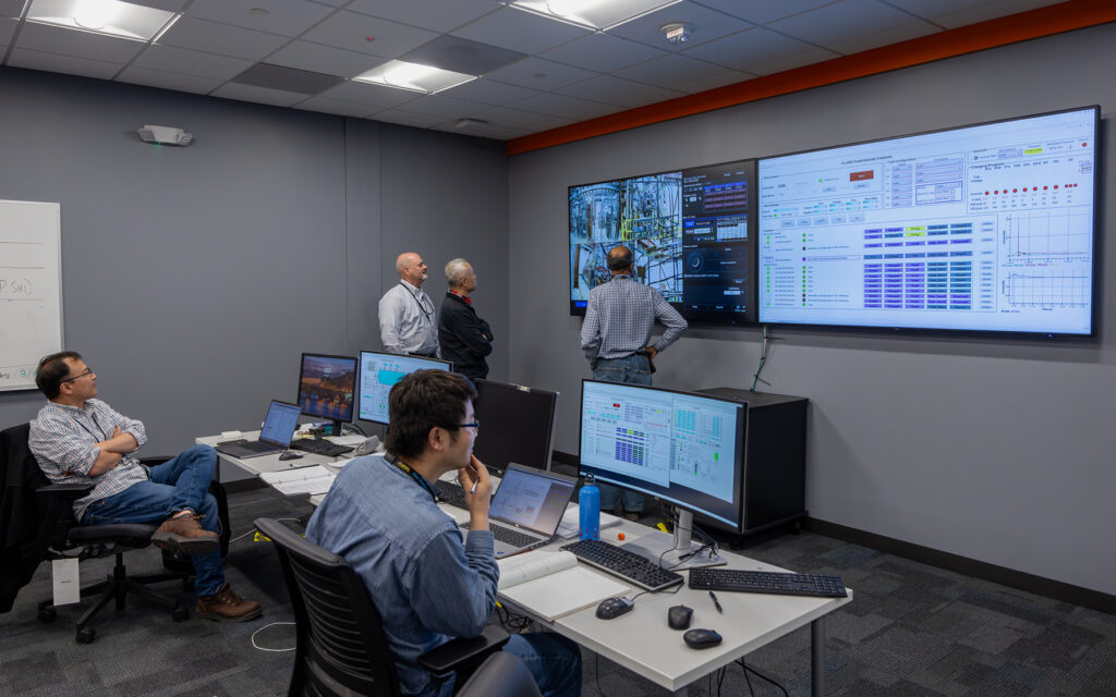 Scientists in a control room looking at data on tv and computer screens