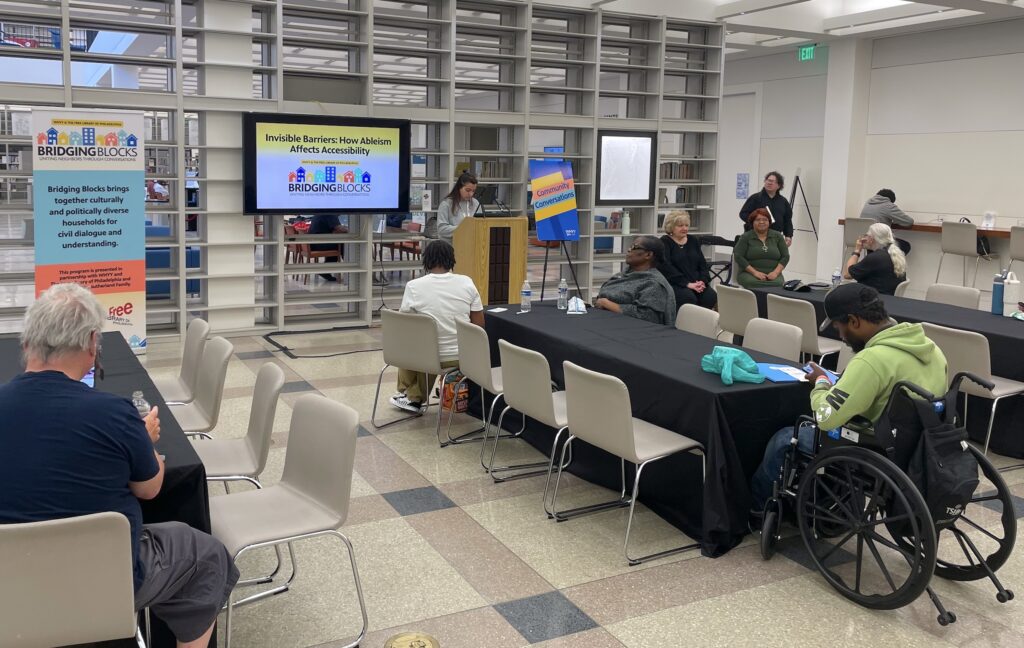 bridging-blocks-accessibility-n-harrington-2025-06-18 People in a room listening to a speaker at a podium