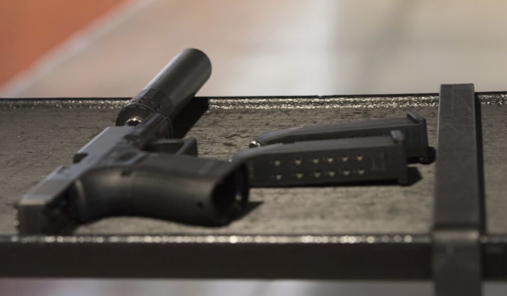 a gun with a silencer attached and two magazines lie on a table