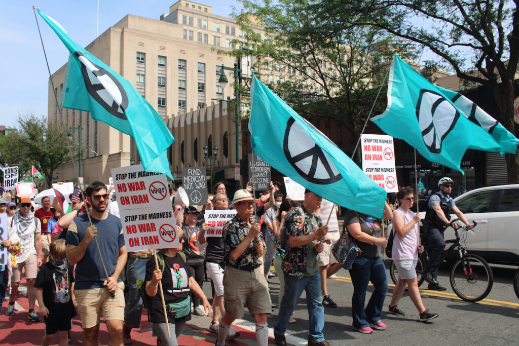 no-war-on-iran-4_copy People march in Philadelphia holding signs and flags with the symbol for peace on them