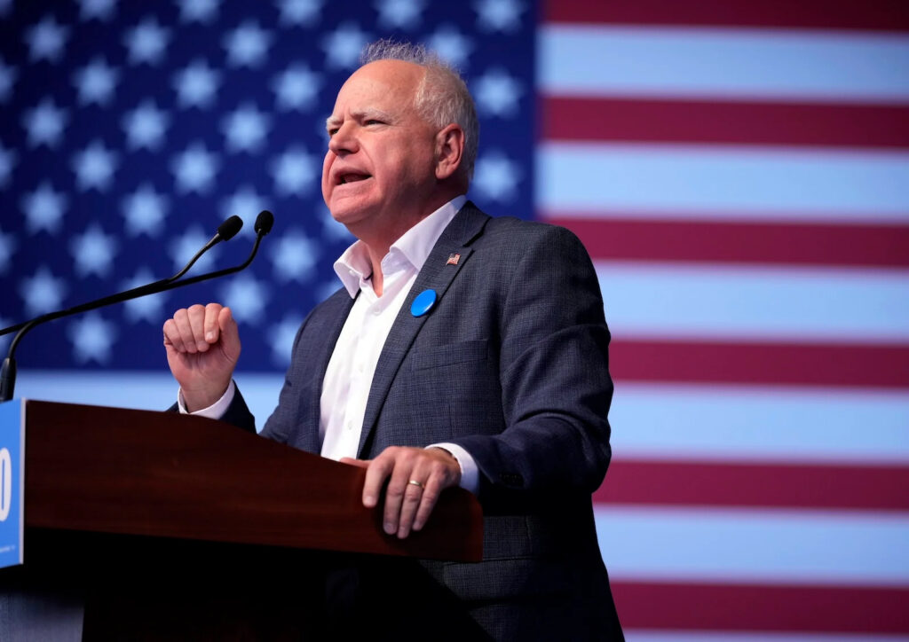 Minnesota Governor Tim Walz stands behind a podium with an American flag in the background