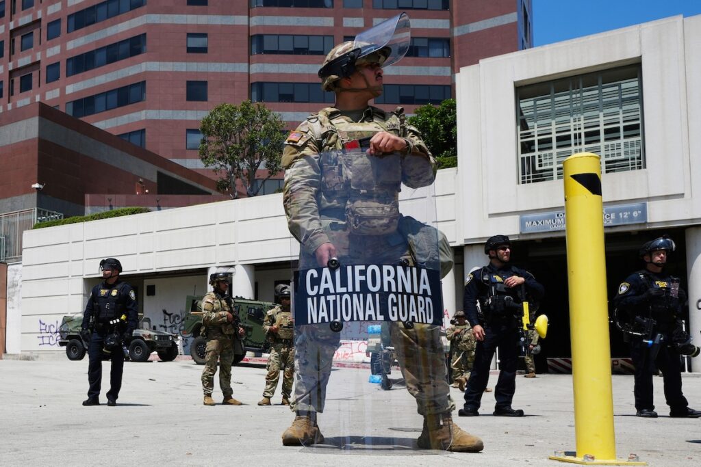 APTOPIX Immigration Raids Los Angeles U.S. National Guard officers stand in full gear, with one officer carrying a riot shield, in Los Angeles