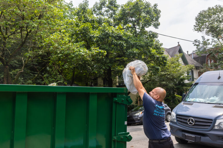 Ray Maldonado throws trash into a temporary dumpster on Queen Lane