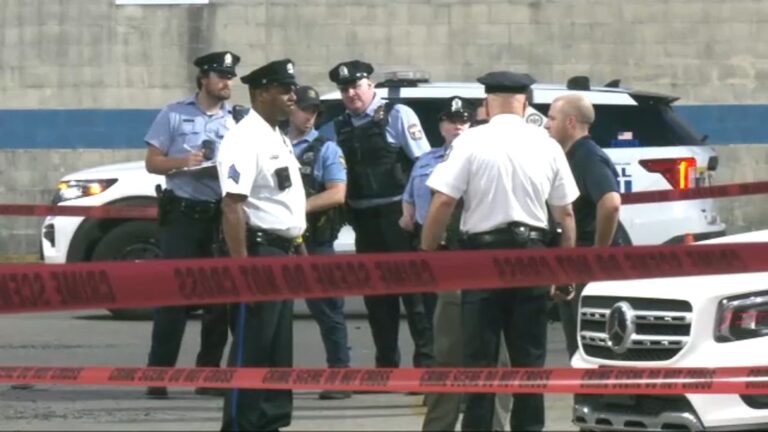 A group of Philadelphia police officers gather in a parking lot behind caution tape
