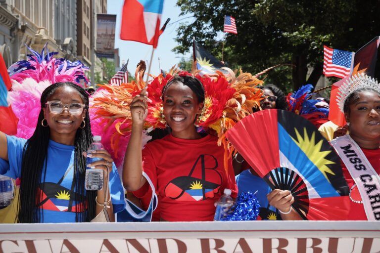 Three women participate in a Fourth of July parade while holding various flags and colorful objects.