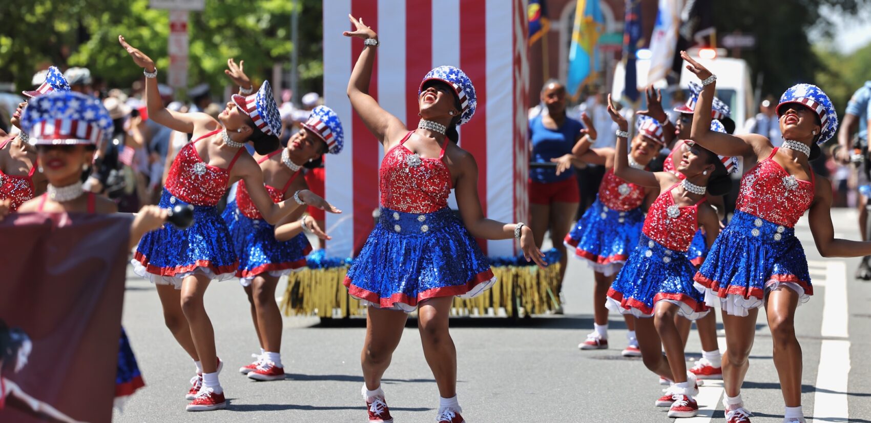 Women wearing American flag-themed dresses dance during the Philadelphia Fourth of July parade.