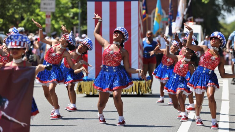 Women wearing American flag-themed dresses dance during the Philadelphia Fourth of July parade.