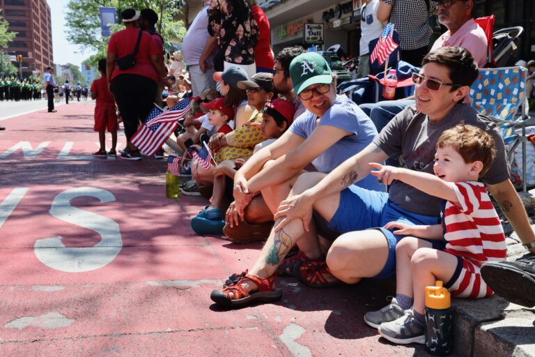 People sit on the sidewalk to watch the Fourth of July parade in Philadelphia.