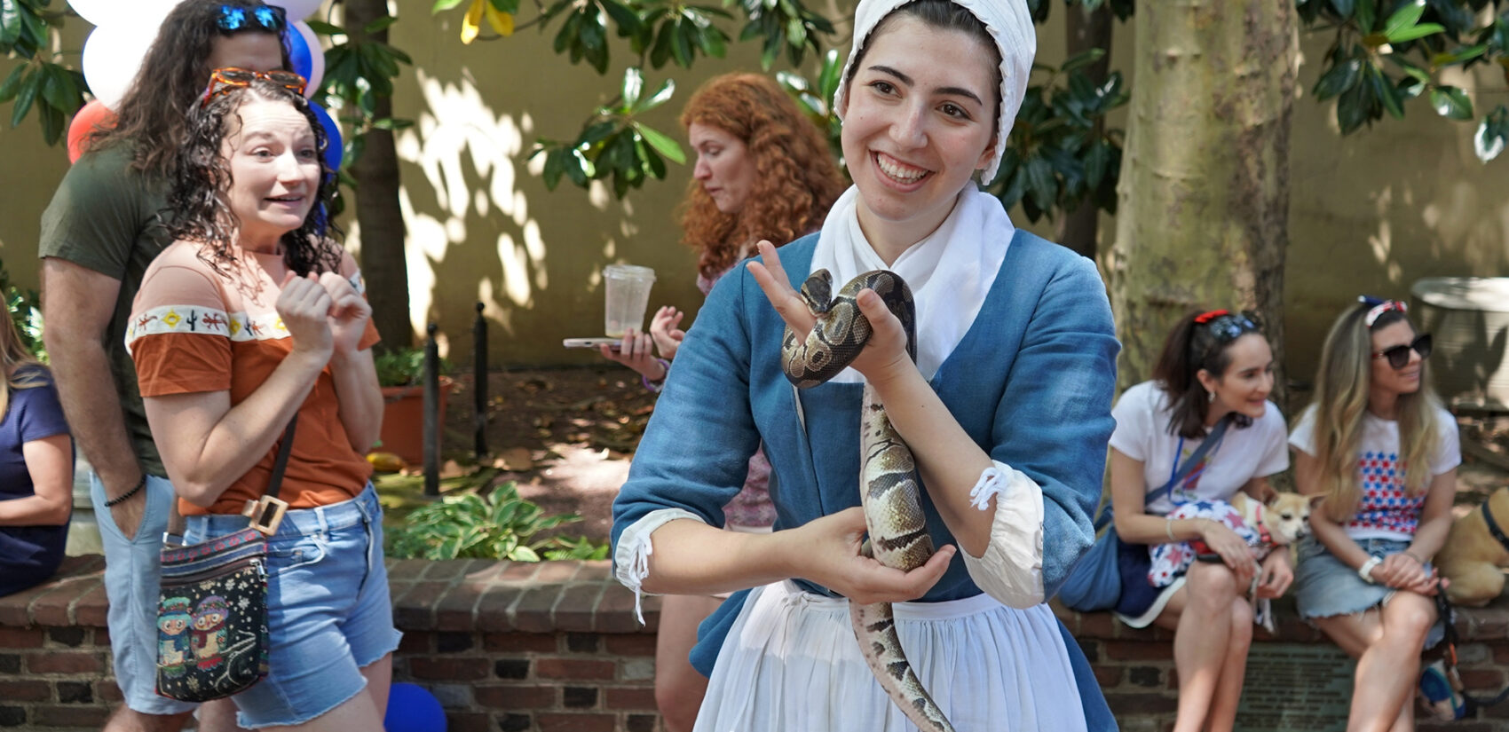 A woman dressed in 18th century garb holds a ball python
