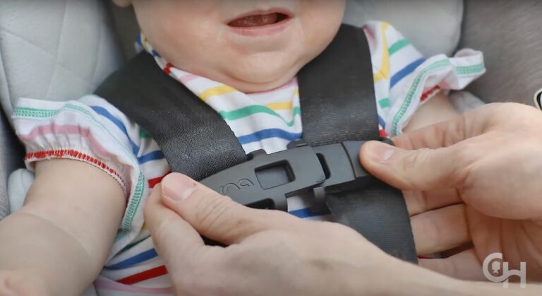 A close-up photo of an adult snapping a child into a car seat