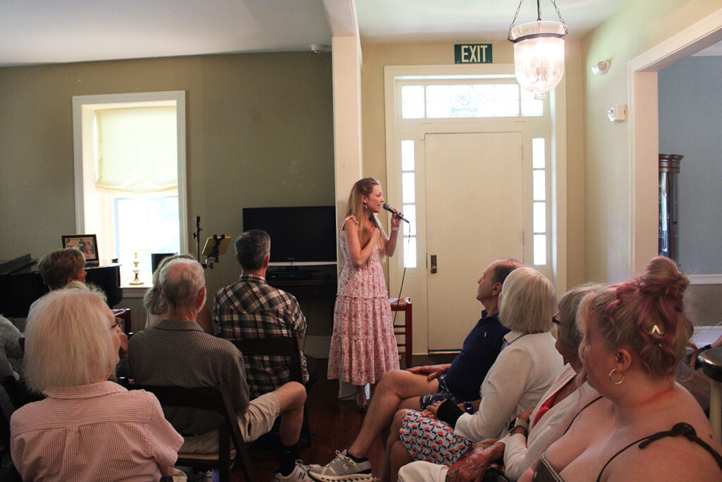 A woman sings in front of a seated audience inside a Doylestown home