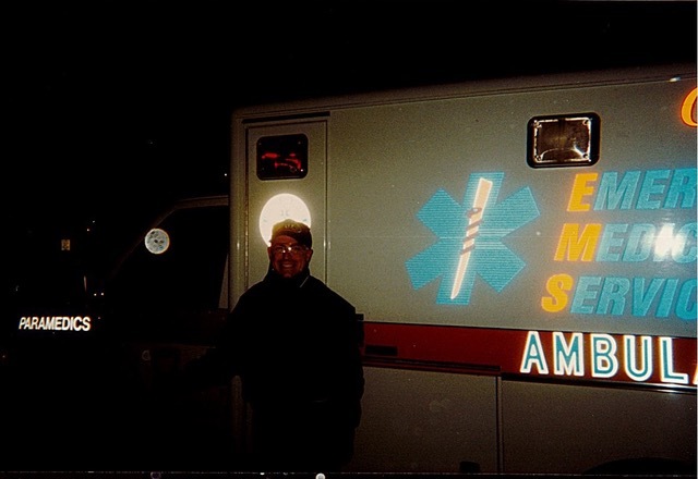 A man posing in front of an ambulance in the evening