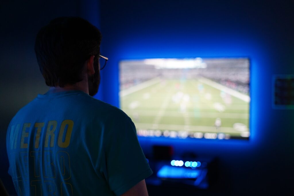 A man stands watching a video game being played on a big screen