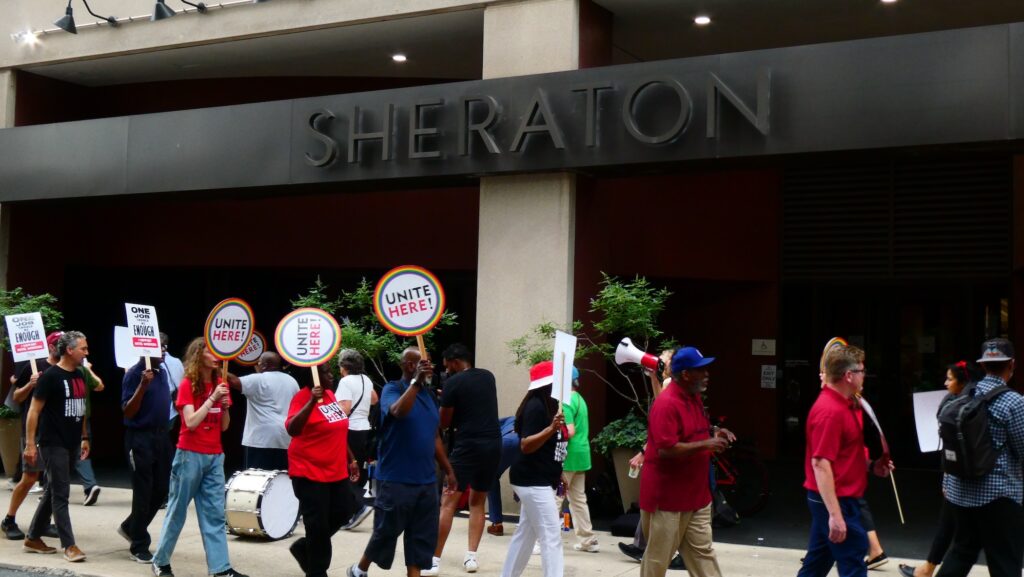 sheraton-workers-protest-c-sharber-2025-07-23-4 Protesters march in front of the entrance to the Sheraton hotel