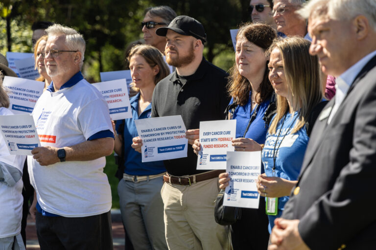 Researchers and cancer survivors hold signs at Independence Hall reading ENABLE CANCER CURES OF TOMORROW BY PROTECTING CANCER RESEARCH TODAY