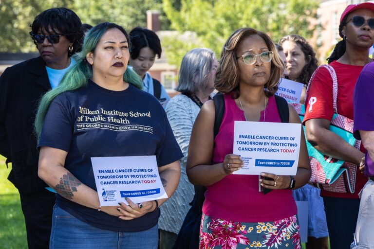 Researchers and cancer survivors hold signs at Independence Hall reading ENABLE CANCER CURES OF TOMORROW BY PROTECTING CANCER RESEARCH TODAY