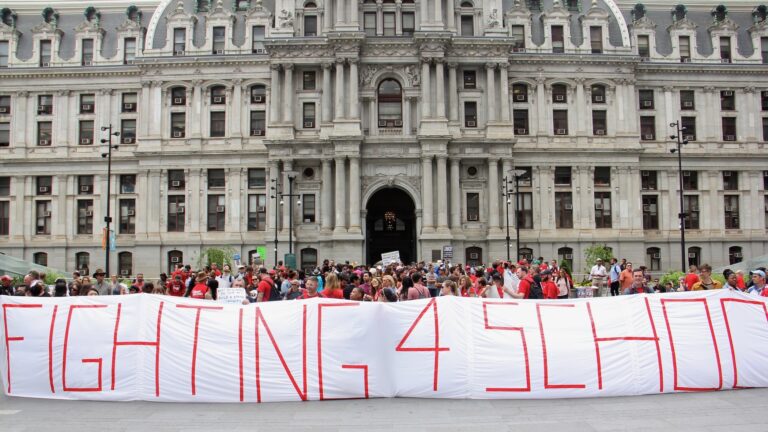 Teachers hold up a large sign in front of City Hall at the protest that reads 'FIGHTING 4 SCHOOLS'