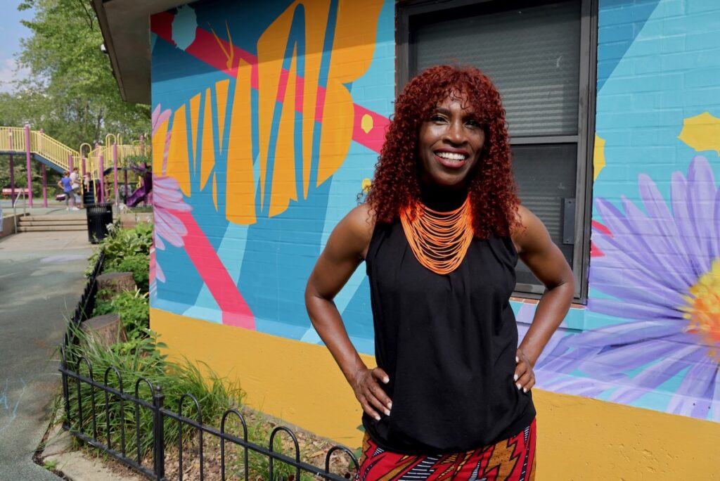 Val Gay poses in front of mural